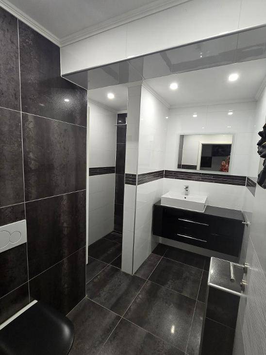 Modernes WC mit dunklen und weißen Fliesen, wandhängendem WC und einem stilvollen Waschbecken.