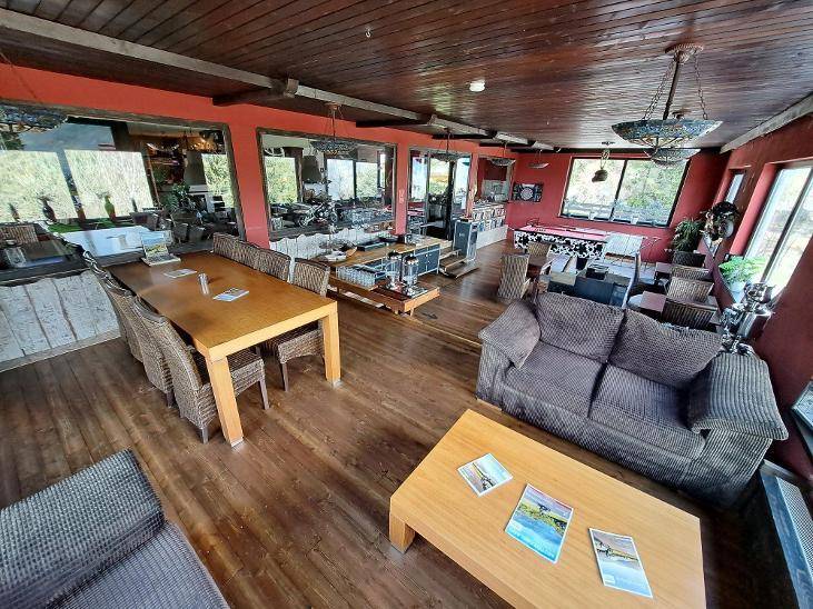 Großer Gemeinschaftsraum mit langem Holztisch, bequemen Sofas und großen Fenstern, die viel Tageslicht hereinlassen.