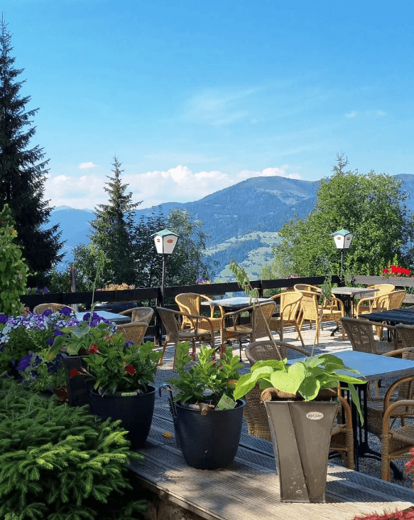 Sonnenterrasse mit Korbmöbeln und Pflanzen, die einen weiten Blick auf die umliegende Berglandschaft bietet.