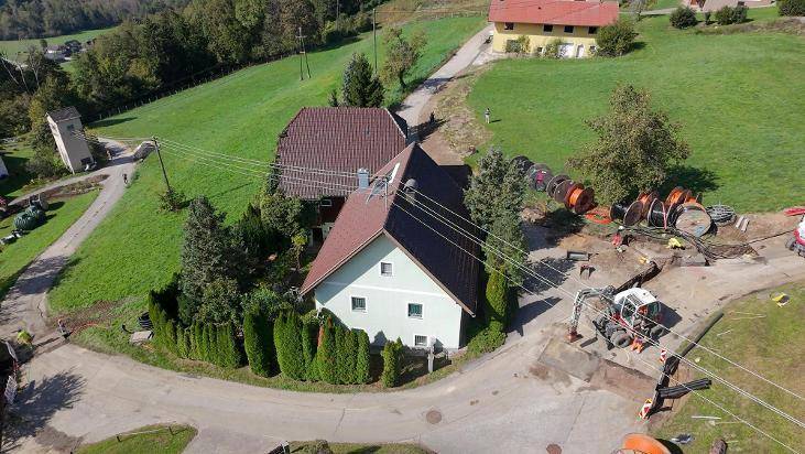 Luftbild des Hauses mit grüner Fassade, umgeben von Bäumen und einer Baustelle im Vordergrund.