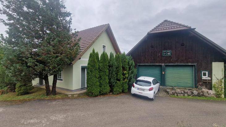 Zwei ländliche Gebäude mit grüner Fassade und Holzverkleidung, umgeben von Bäumen.