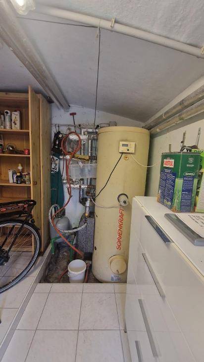 Hauswirtschaftsraum mit großem Warmwasserspeicher, Regalen und Fliesenboden.