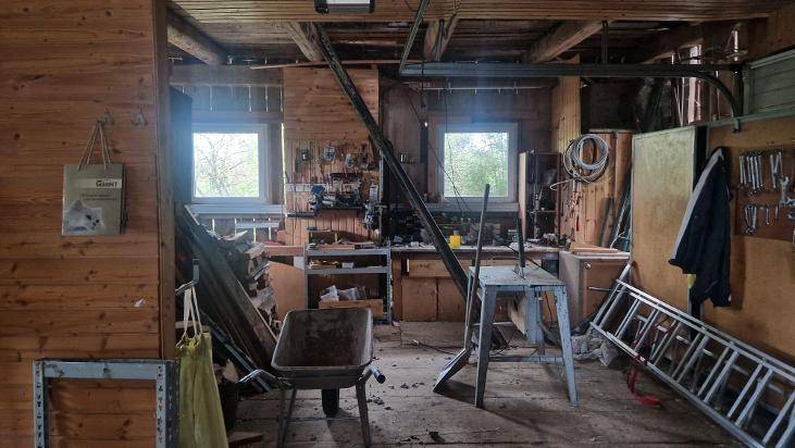 Rustikaler Werkstattraum mit Holzwänden, Werkzeugen und zwei kleinen Fenstern.