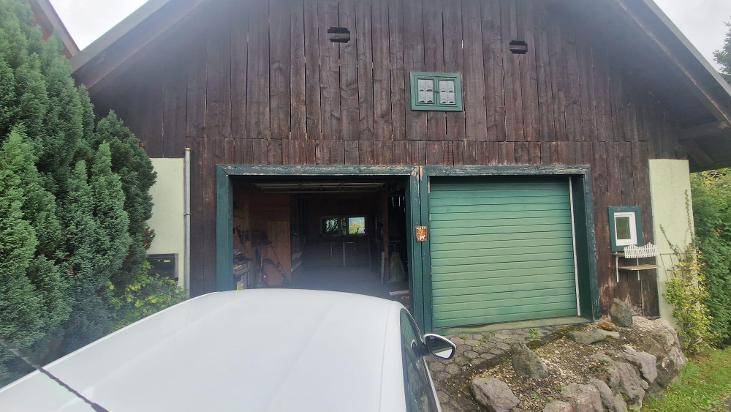 Offene Garage mit grünen Toren und Blick ins Innere, neben einem geparkten Auto.