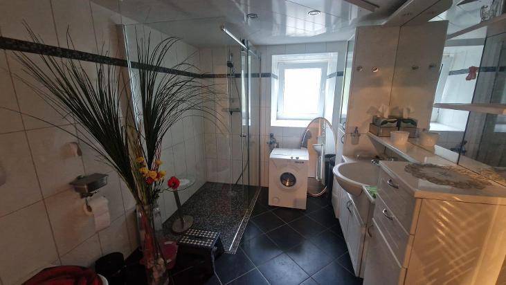 Modernes Badezimmer mit Dusche, Waschbecken und Waschmaschine, dunklem Fliesenboden.