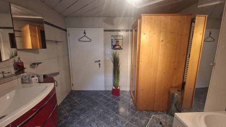 Badezimmer mit Waschbecken, Spiegel und einer integrierten Sauna, gefliestem Boden.