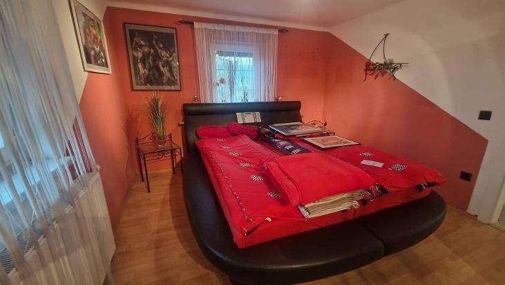 Schlafzimmer mit roter Wand, Doppelbett und Dachschräge, gemütlich eingerichtet.