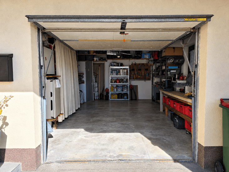 Geräumige Garage mit Betonboden, Regalen und Werkbank, auch als Werkstatt nutzbar.