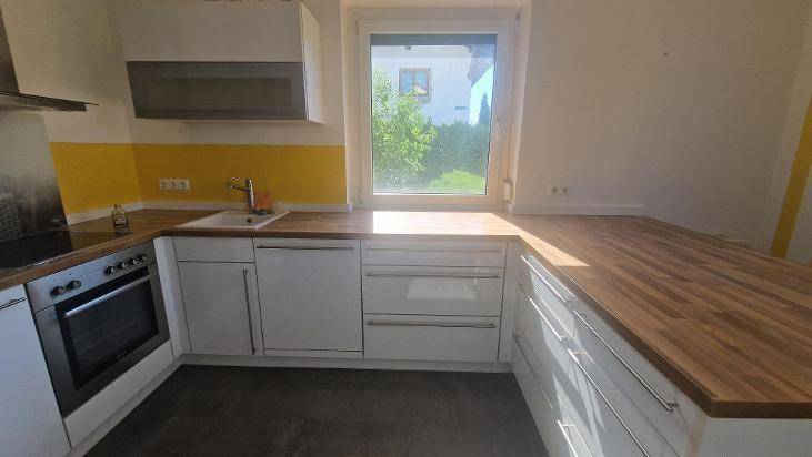 Moderne Küche mit weißen Fronten, Holzarbeitsplatten und gelbem Fliesenspiegel.