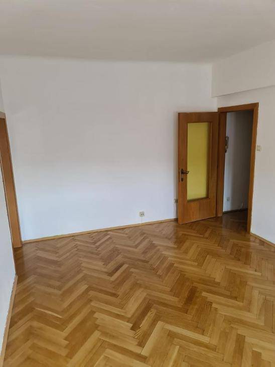 Heller Raum mit klassischem Fischgrätparkett und einer Holztür mit Glaseinsatz.