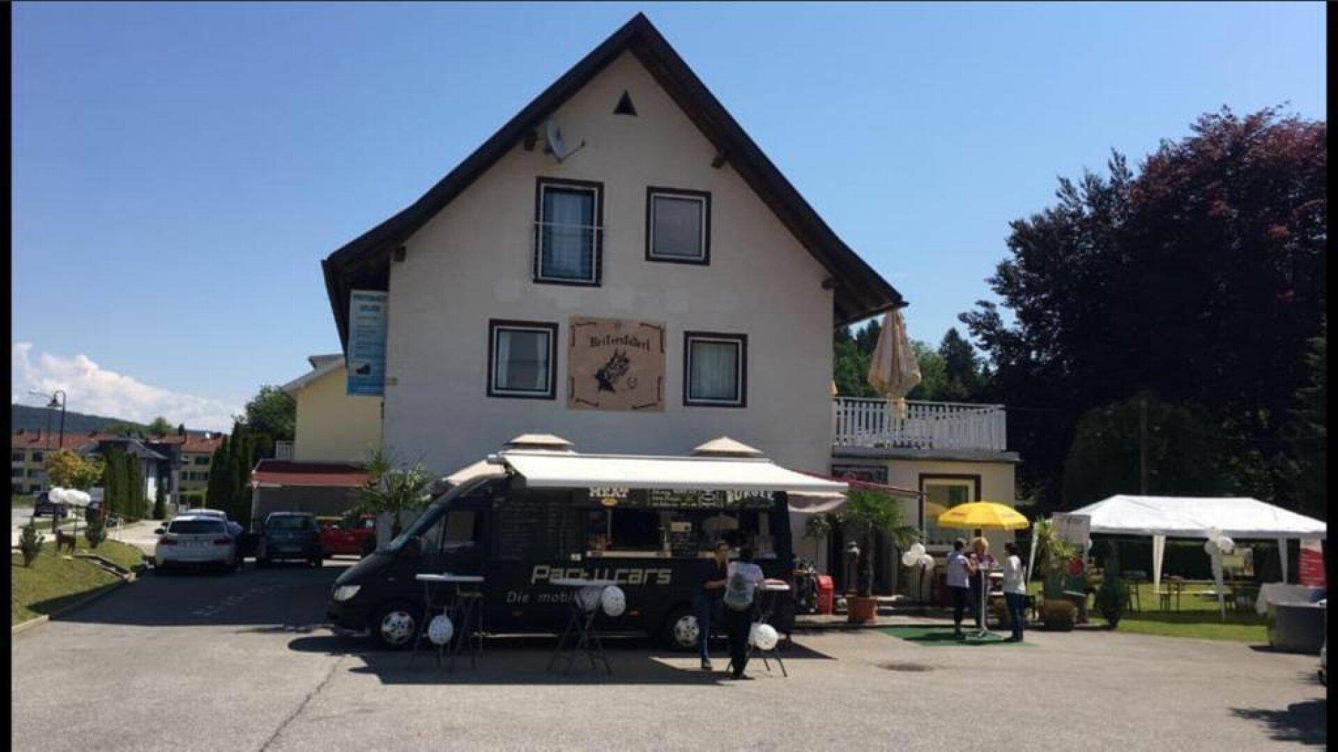 Gebäude mit Foodtruck und Außenbereich für Gäste an einem sonnigen Tag.