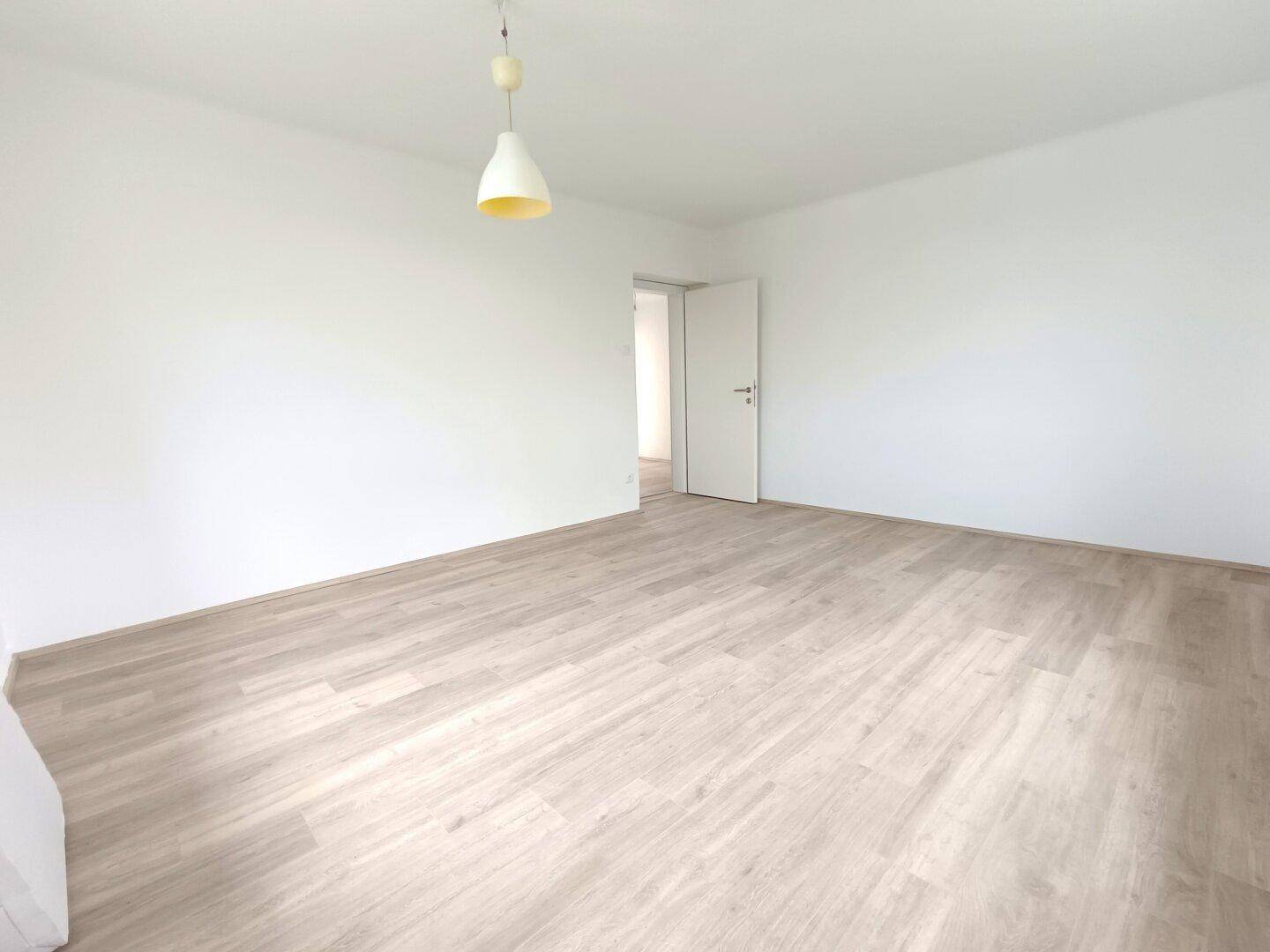 Geräumiges Zimmer mit hellem Laminatboden und weiß gestrichenen Wänden, bereit zur Einrichtung.
