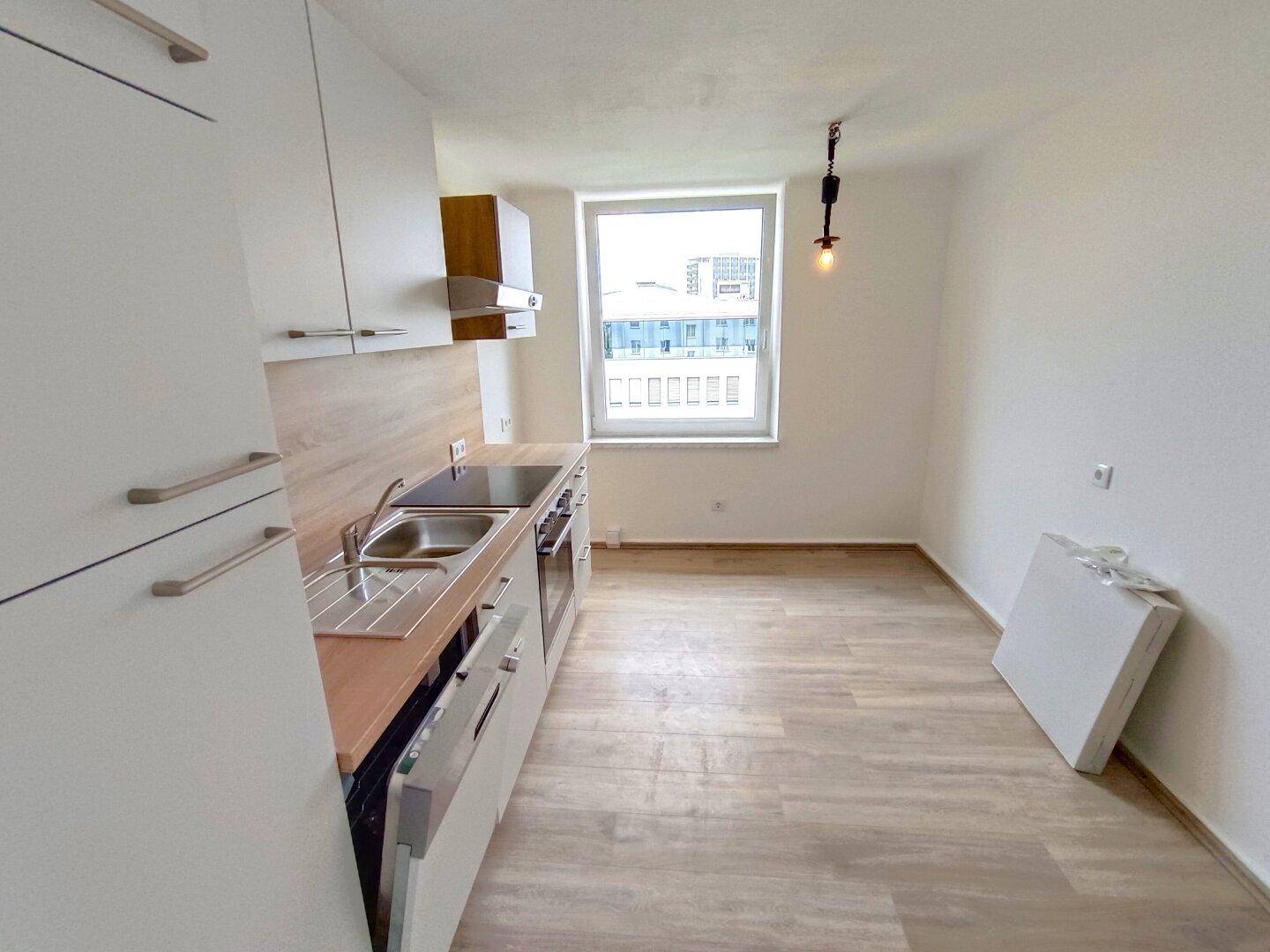 Funktionale Küche mit weißen Fronten, Holzdetails und Fenster mit Blick auf die Stadt.