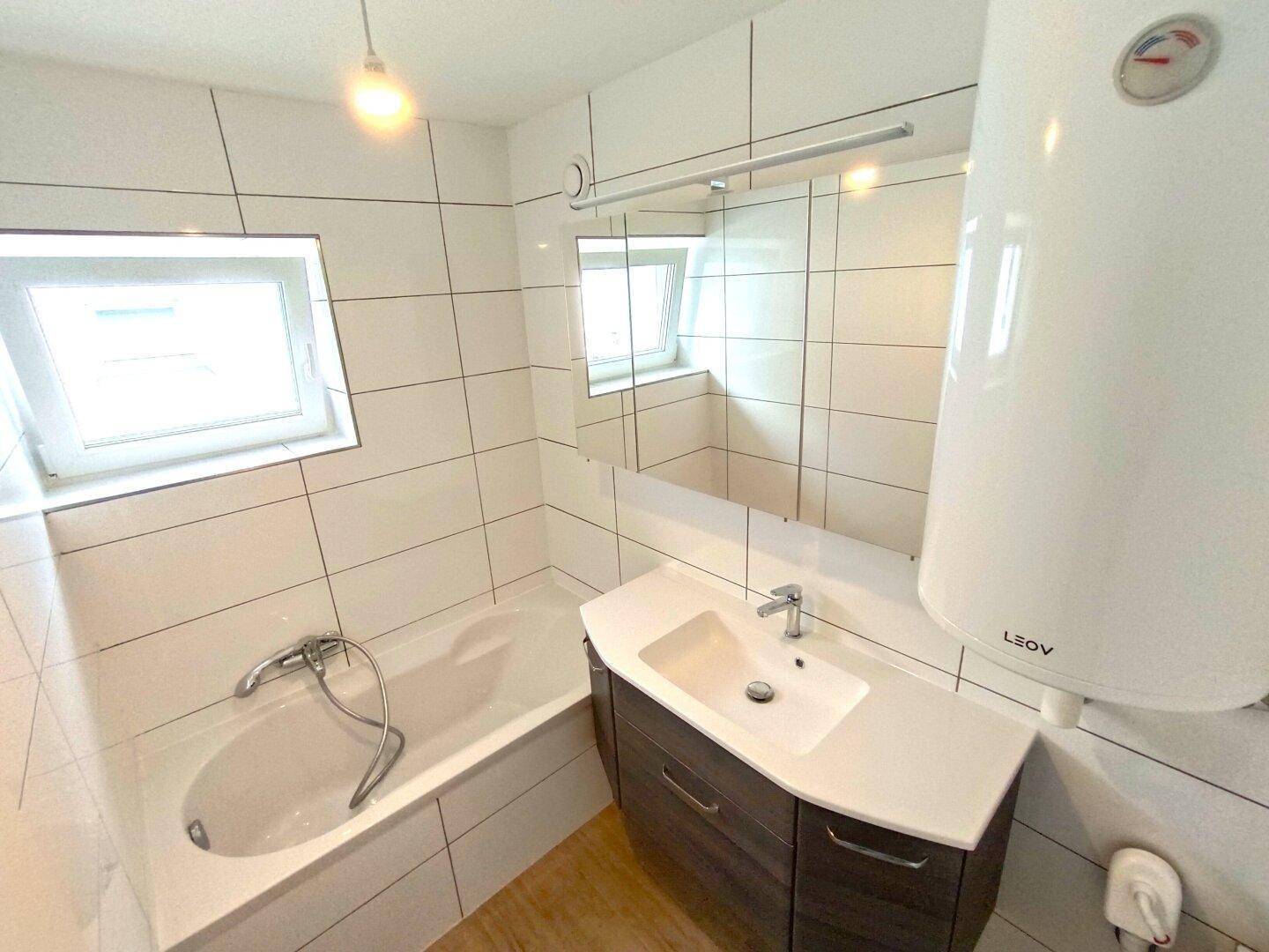 Modern gefliestes Badezimmer mit Badewanne, Waschtisch und Fenster für Tageslicht.