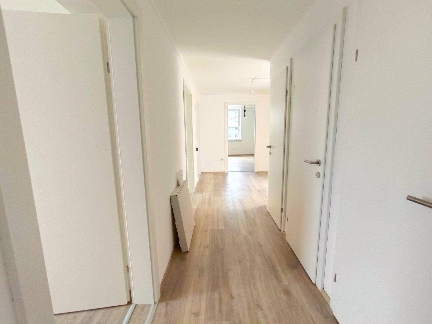 Langer, heller Flur mit Laminatboden und mehreren Türen, der verschiedene Räume verbindet.