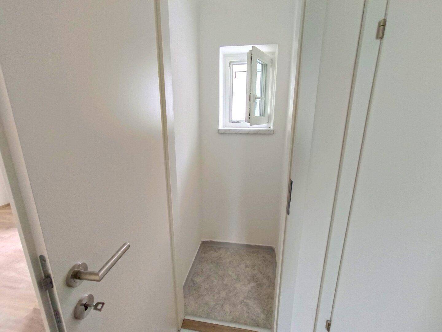 Kleiner Abstellraum mit Fenster und Teppichboden, ideal für zusätzlichen Stauraum.
