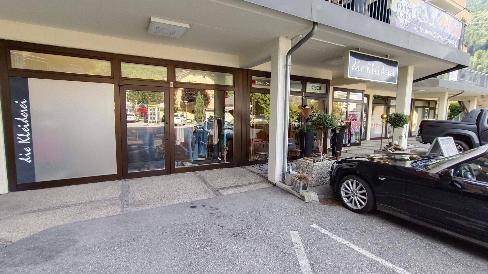 Vorderansicht eines Geschäftsgebäudes mit großen Schaufenstern und einem geparkten schwarzen Auto davor.