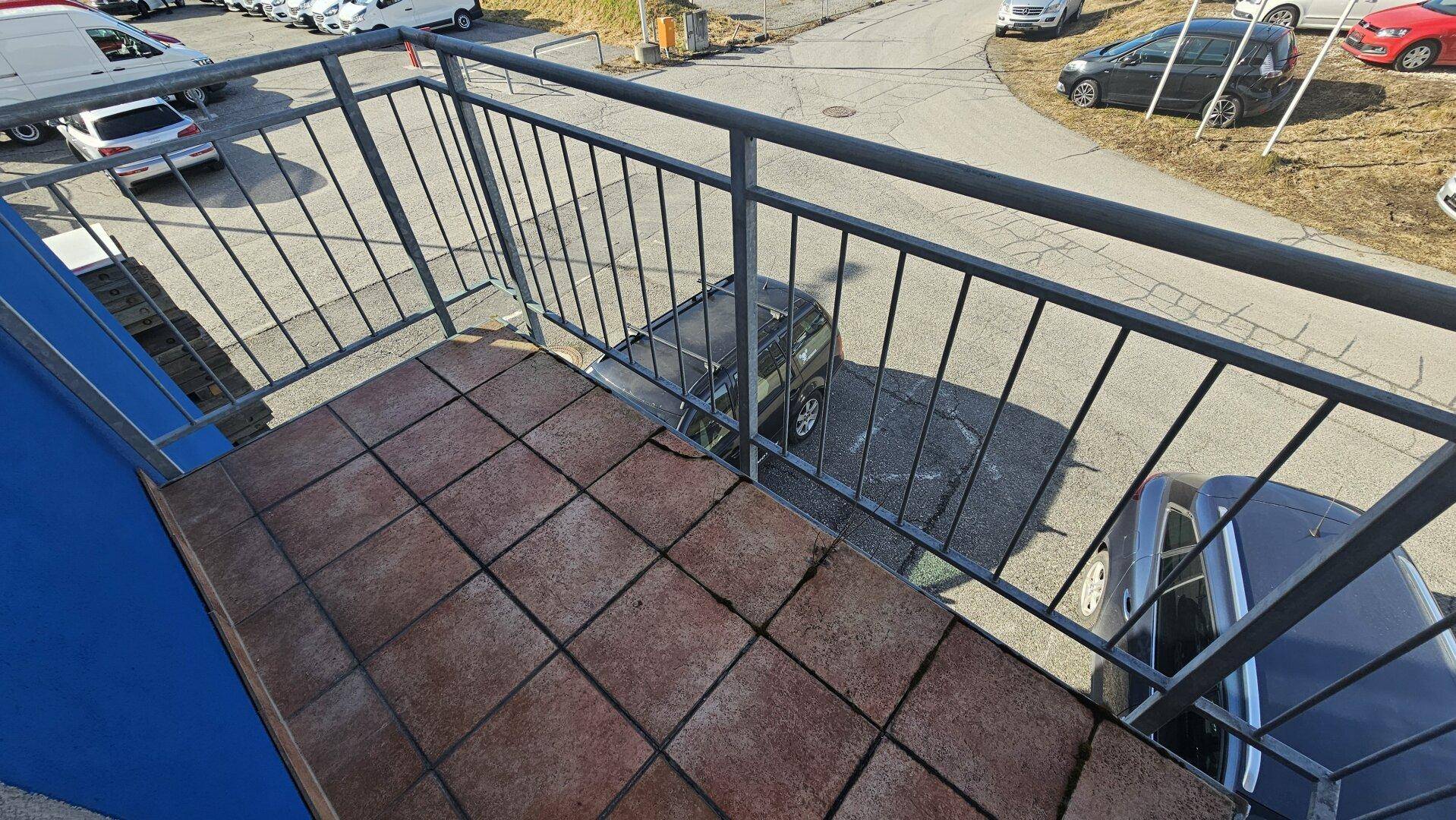 Kleiner Balkon mit Fliesenboden und Metallgeländer, bietet Blick auf den Parkplatz und die Umgebung.