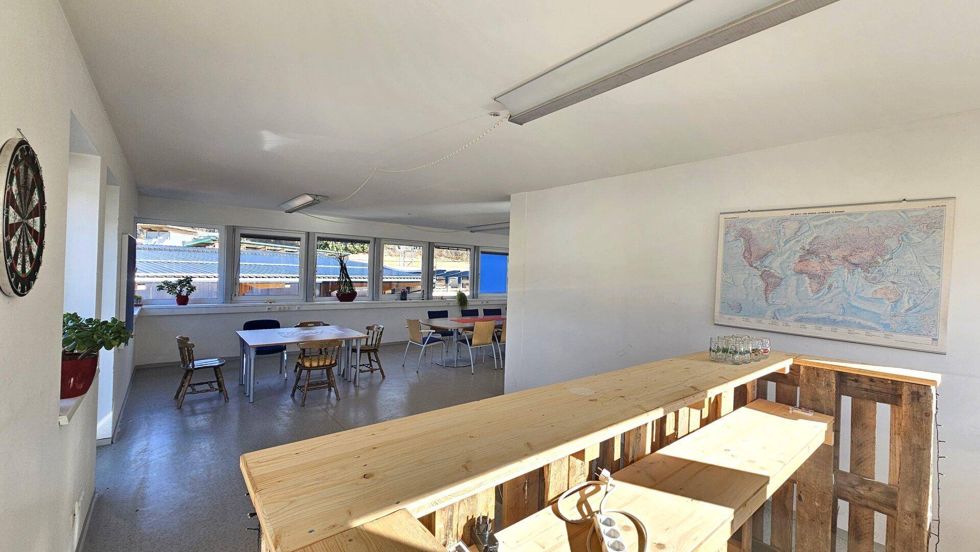 Heller Mehrzweckraum mit einer rustikalen Holzbar und Weltkarte an der Wand, ideal für informelle Treffen.