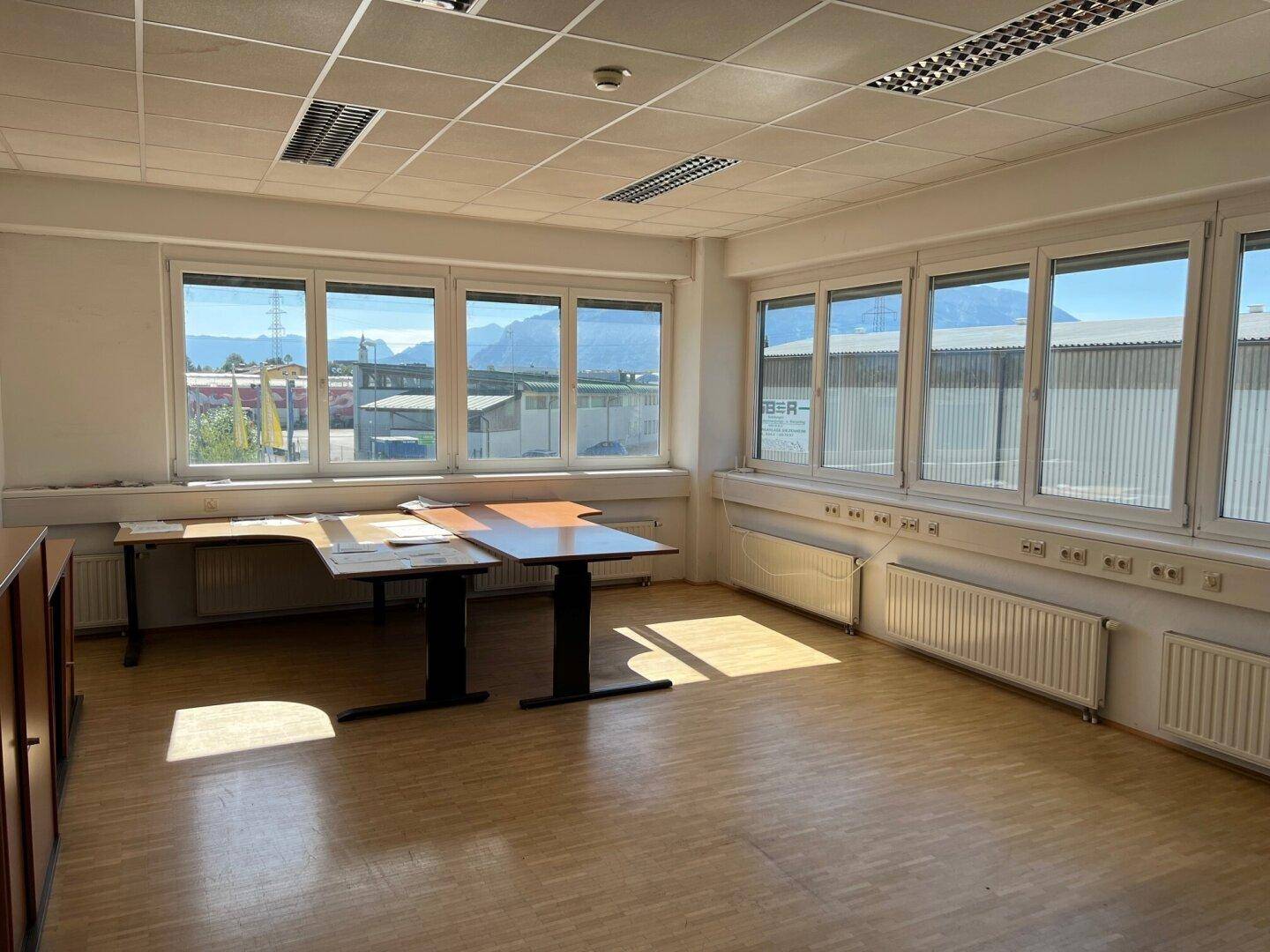 Heller Büroraum mit Holzfußboden, großen Fenstern und Blick auf die Berge.