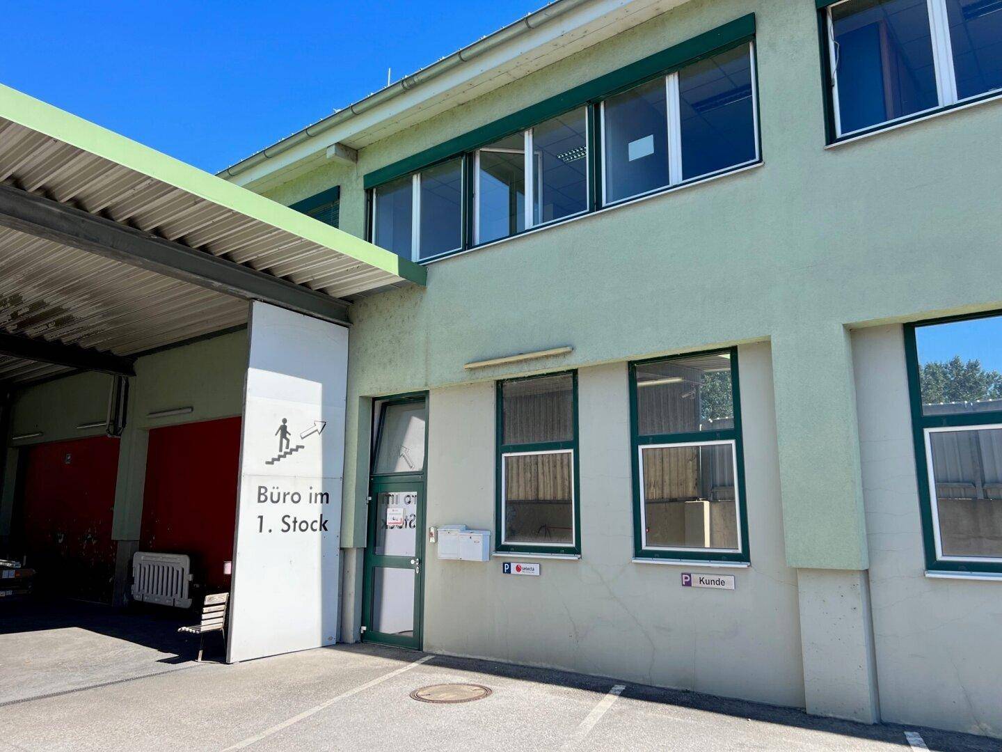 Außenansicht eines Bürogebäudes mit grüner Fassade und Parkplätzen für Kunden.