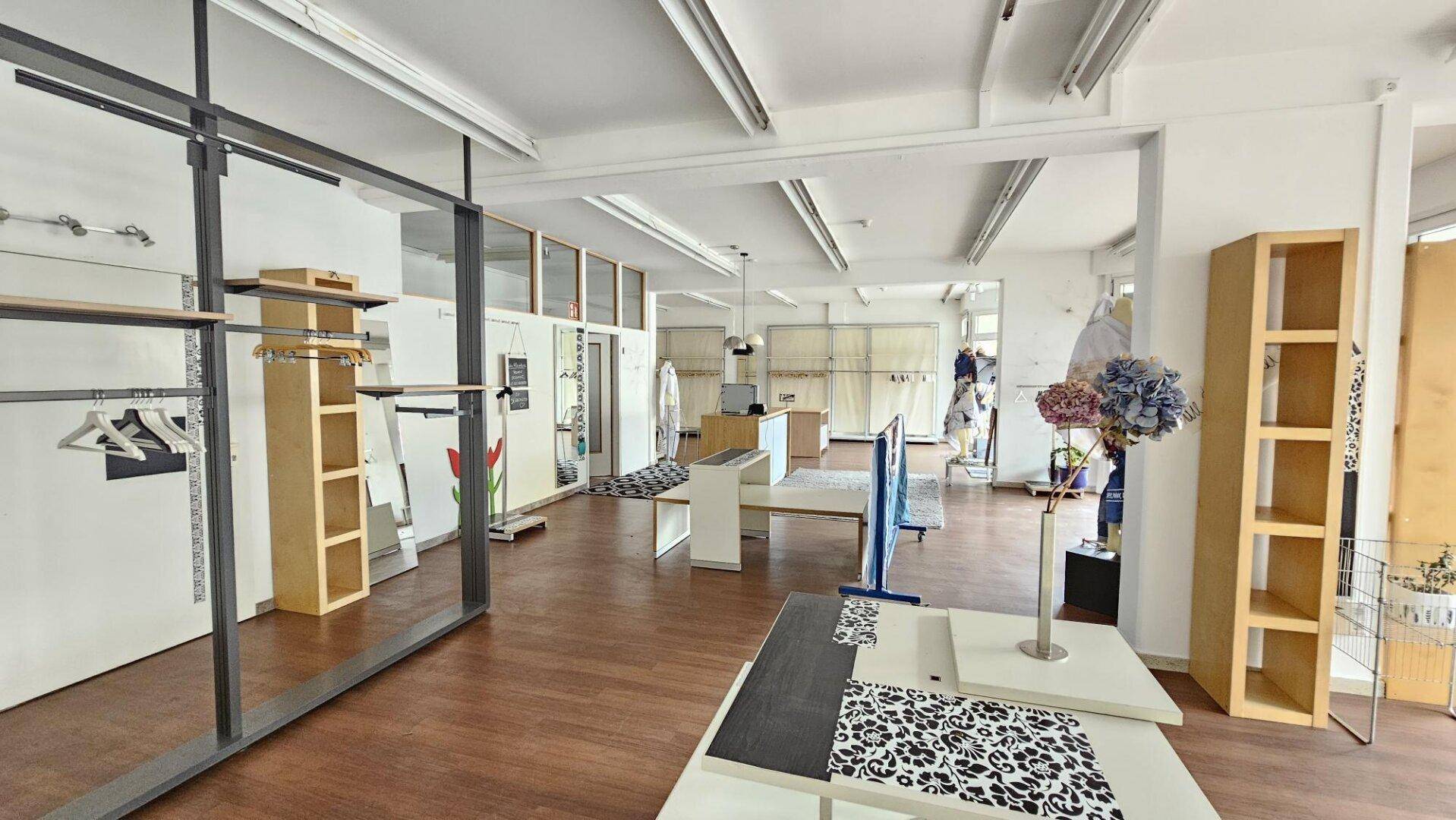 Geräumiger Verkaufsraum mit Holzboden, modernen Regalen und viel Tageslicht, ideal für ein Geschäft.