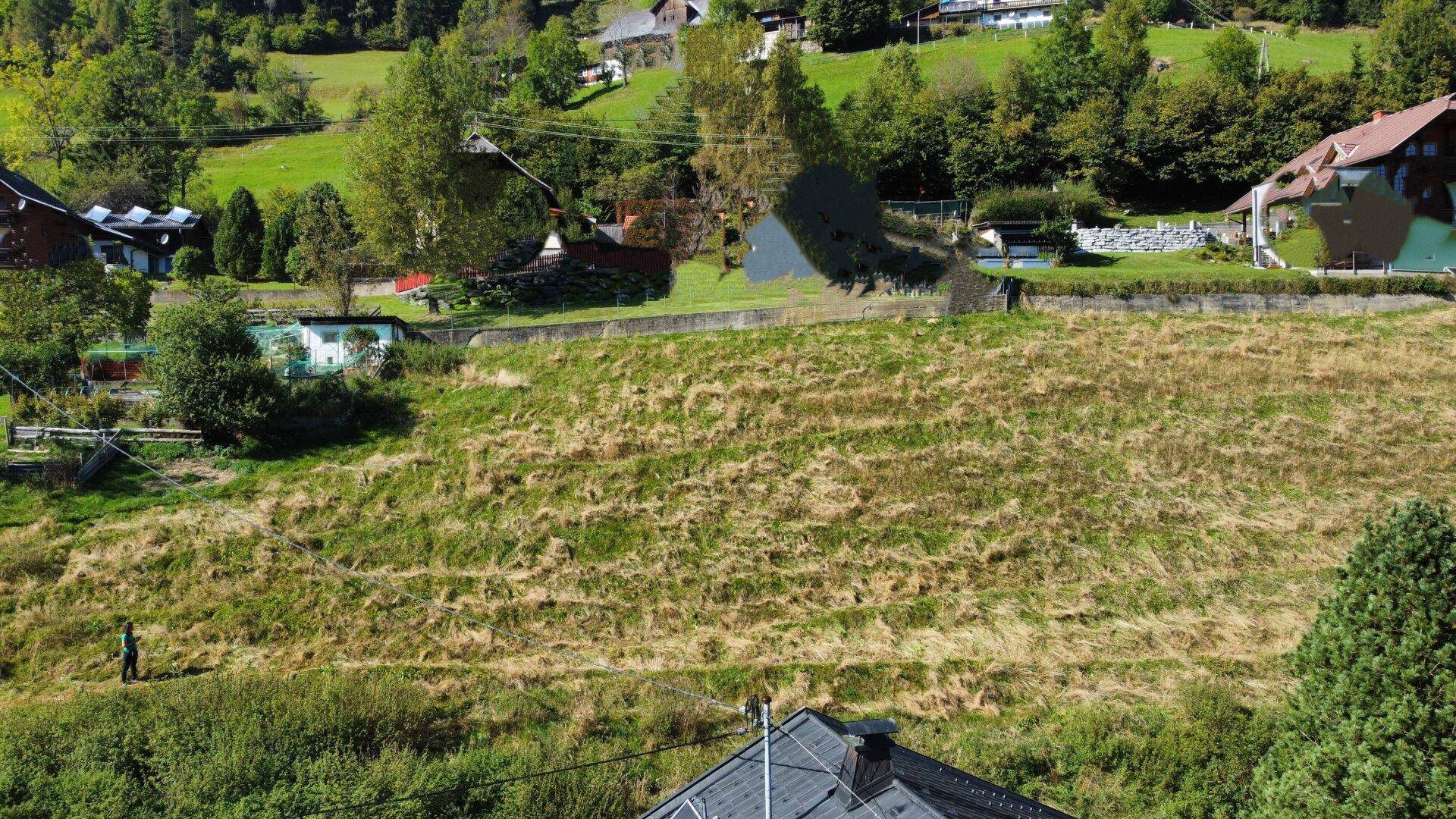 Übersicht des grasbewachsenen Grundstücks mit angrenzenden Häusern und grünen Hügeln in ländlicher Umgebung.