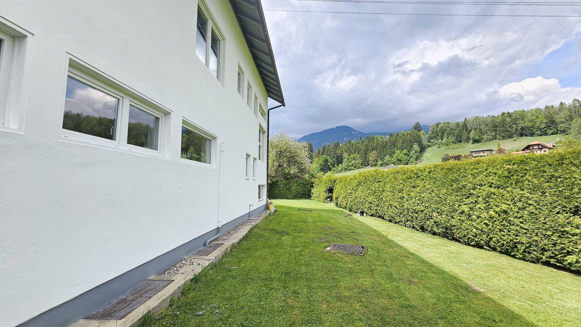 Seitenansicht des Hauses mit grünem Rasen und Blick auf die umliegende Berglandschaft.
