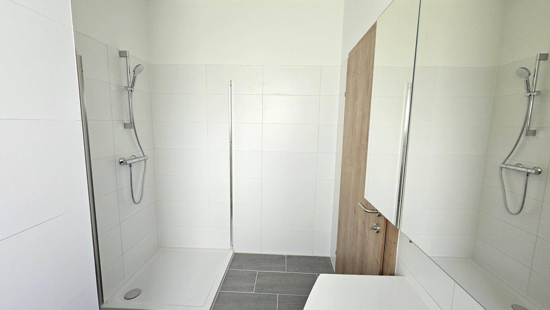Helles Badezimmer mit weiß gefliesten Wänden, grauen Bodenfliesen und einer modernen Duschkabine.