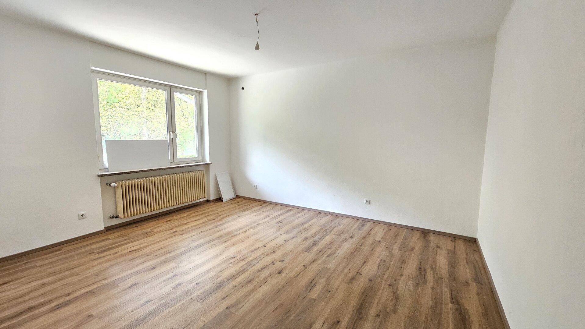 Geräumiges, helles Zimmer mit Laminatboden und einem großen Fenster, das viel Licht spendet.