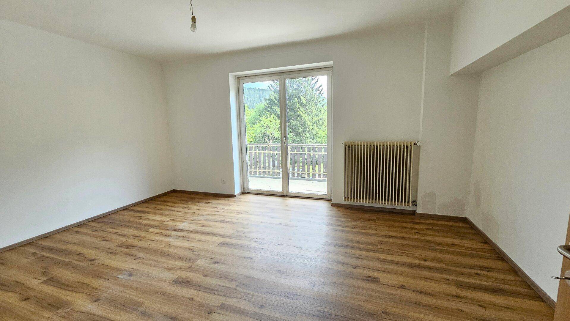 Helles Schlafzimmer mit Laminatboden und direktem Zugang zu einem Balkon mit Blick ins Grüne.