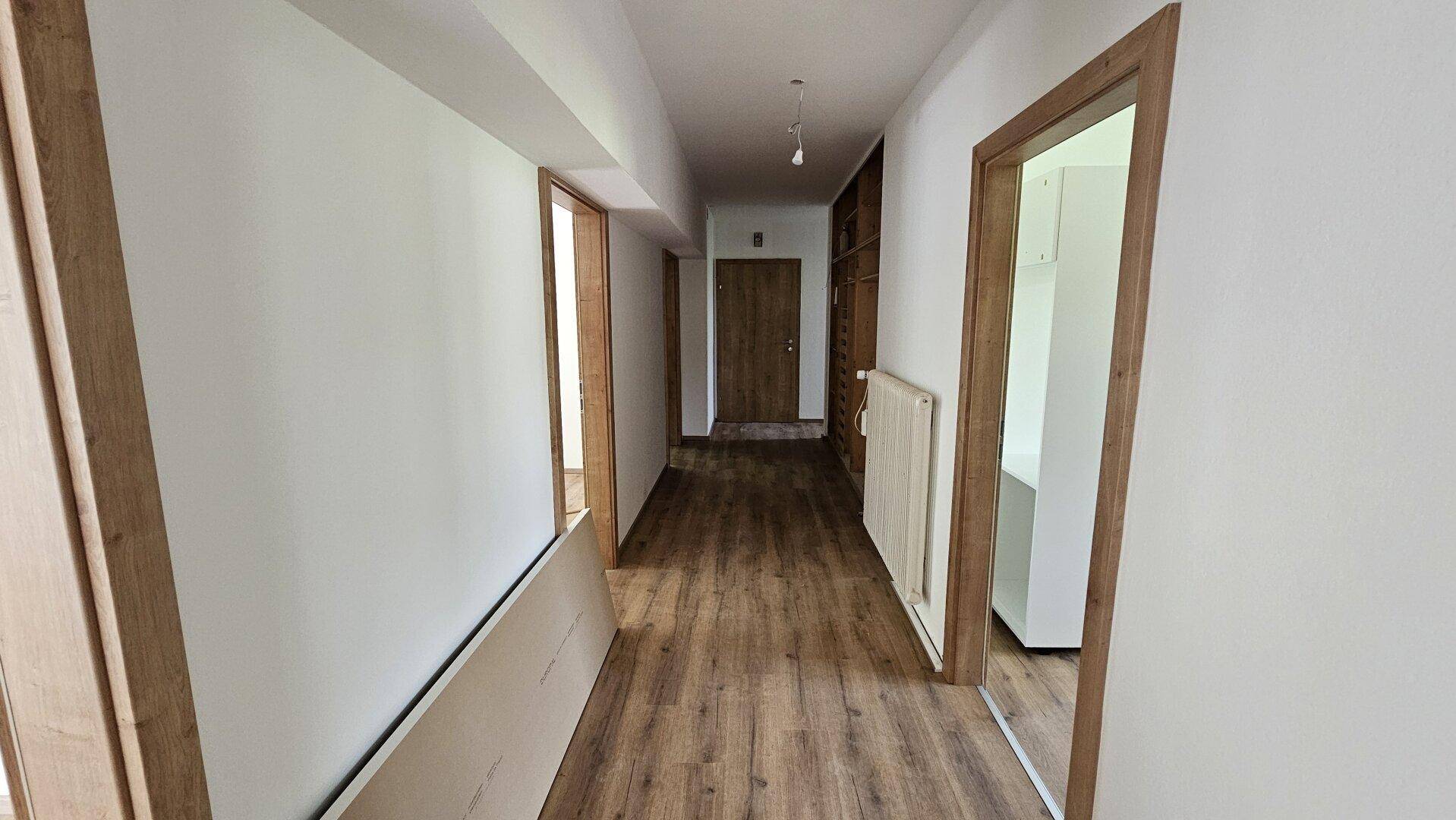 Heller Flur mit Laminatboden und mehreren Holztüren, der die verschiedenen Räume verbindet.