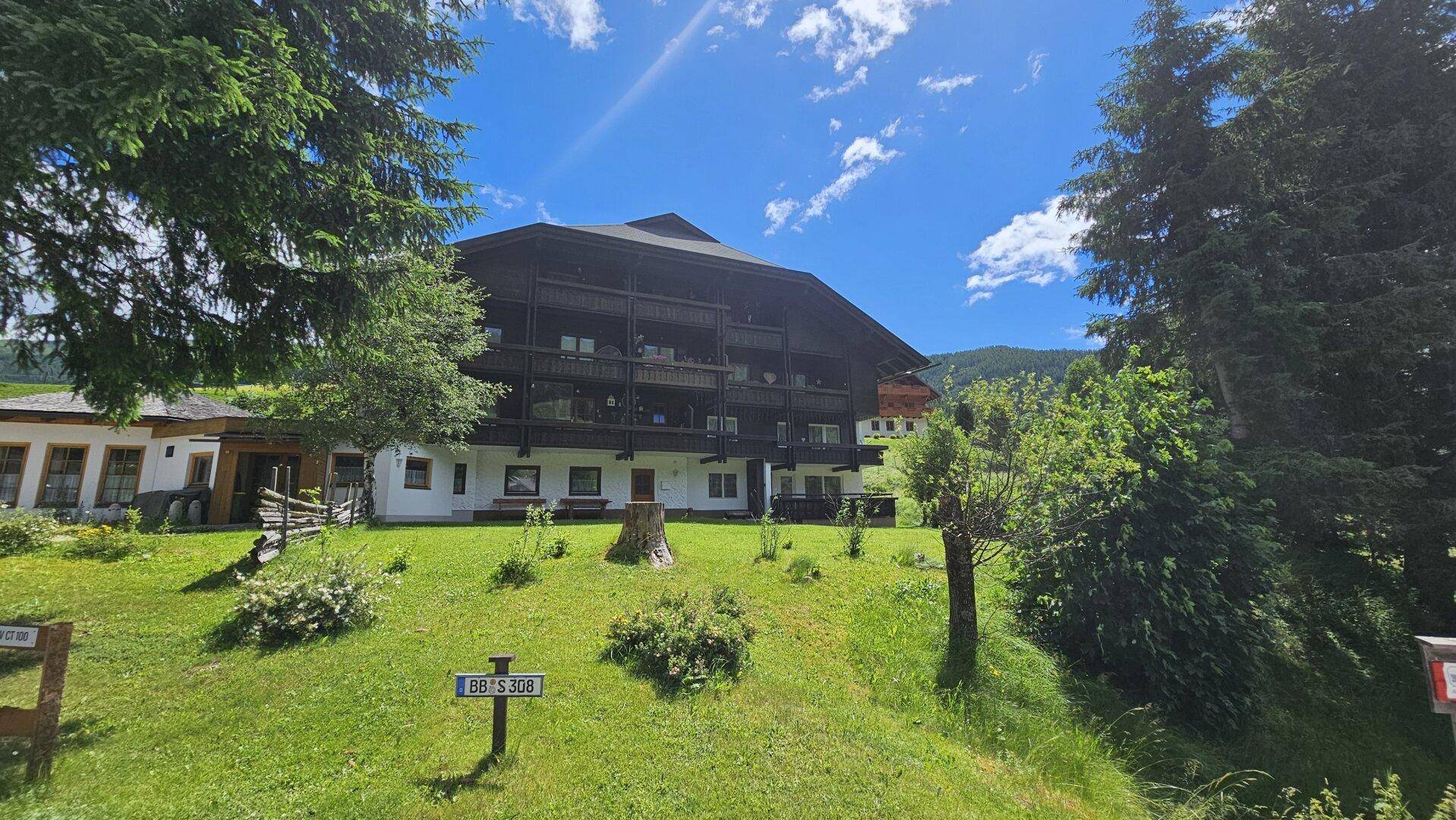 Traditionelles Gebäude mit mehreren Balkonen, umgeben von grüner Natur und Bäumen.