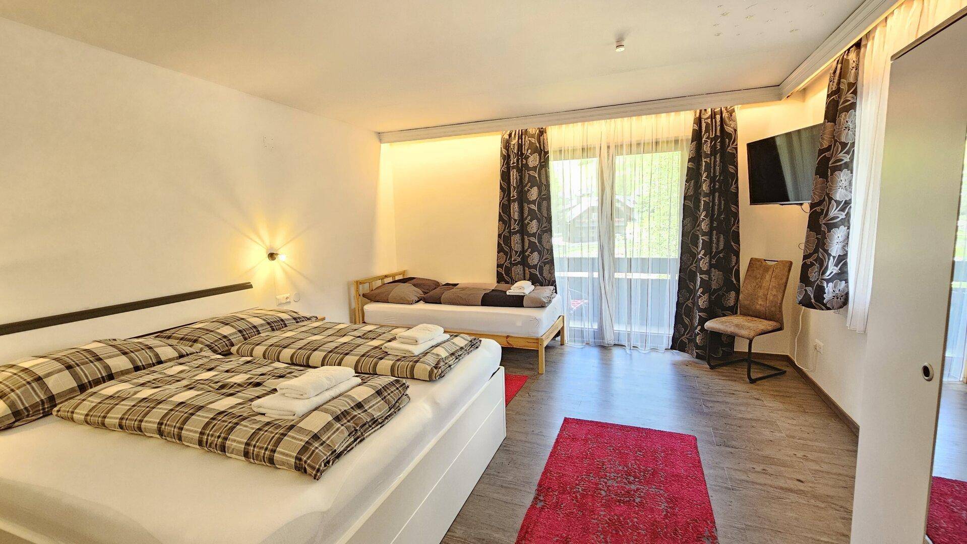 Helles Schlafzimmer mit Doppelbett, Einzelbett und Zugang zum Balkon.