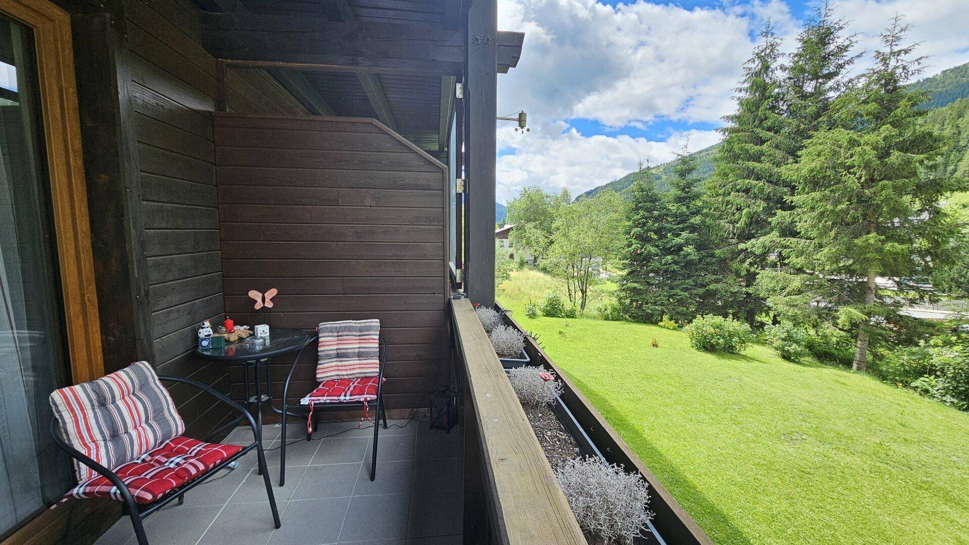 Balkon mit Sitzgelegenheiten und weitem Blick auf die grüne Landschaft und Berge.