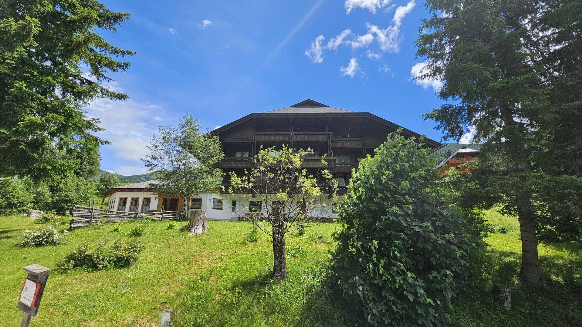 Charmantes Gebäude in alpiner Umgebung, umgeben von üppiger Vegetation und Bäumen.