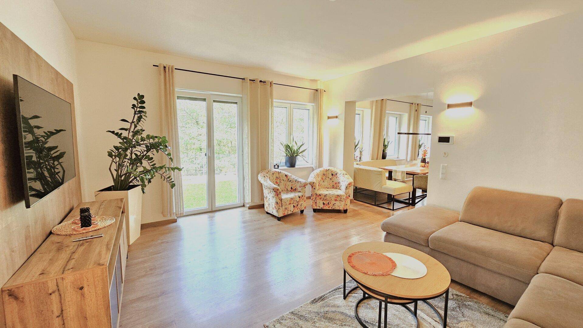 Gemütliches Wohnzimmer mit Holzboden, Sofa und Zugang zum Garten.