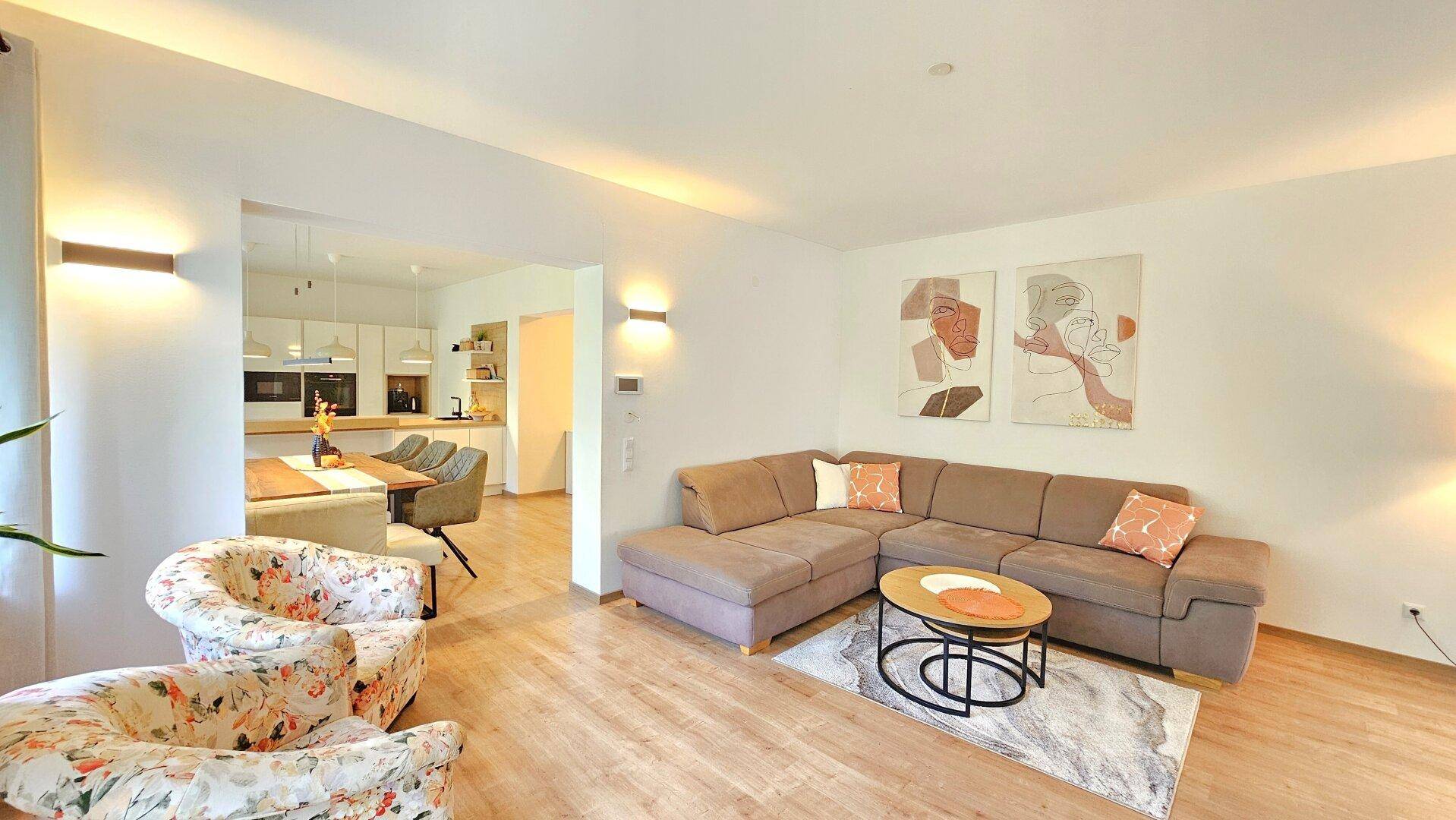 Offener Wohnbereich mit beigem Sofa, Holzboden und Blick zur Küche.