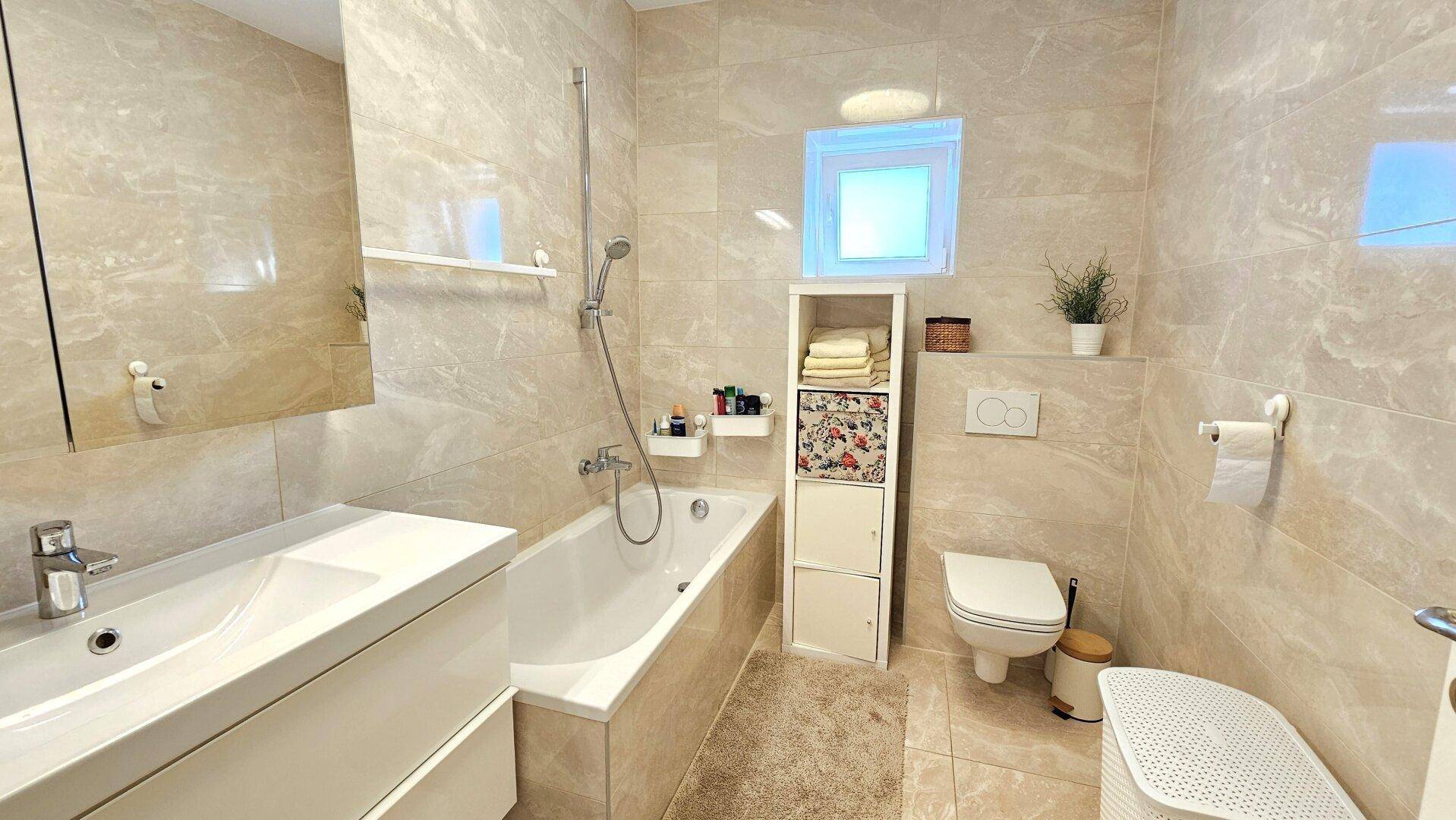 Modernes Badezimmer mit beigen Fliesen, Badewanne und Fenster.