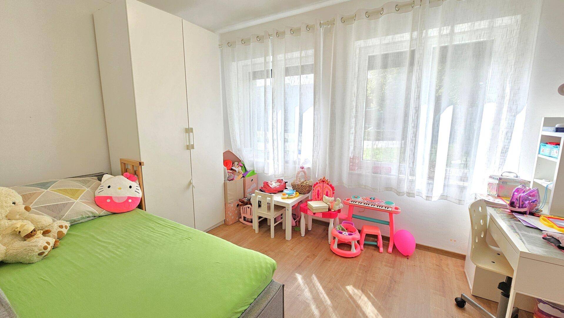 Helles Kinderzimmer mit Holzboden, Spielzeug und großen Fenstern.