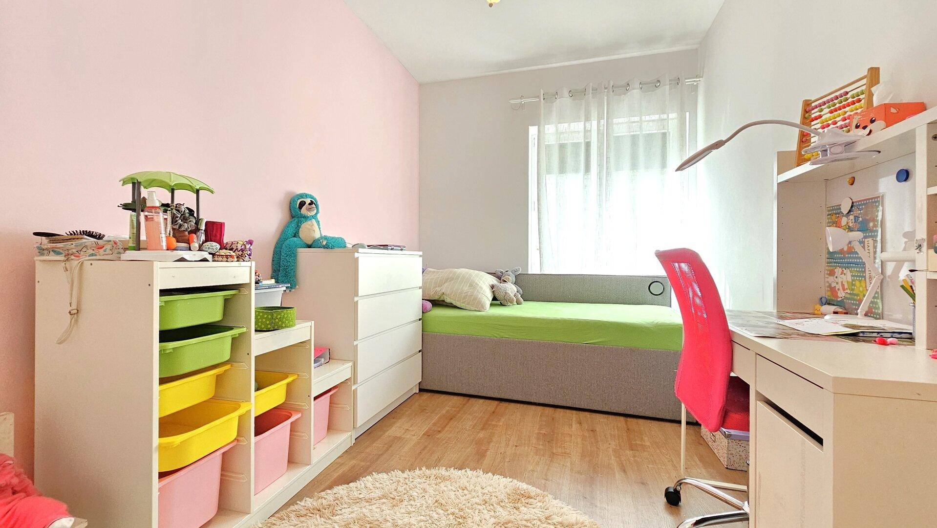 Freundliches Kinderzimmer mit rosa Wand, Holzboden und Schreibtisch.