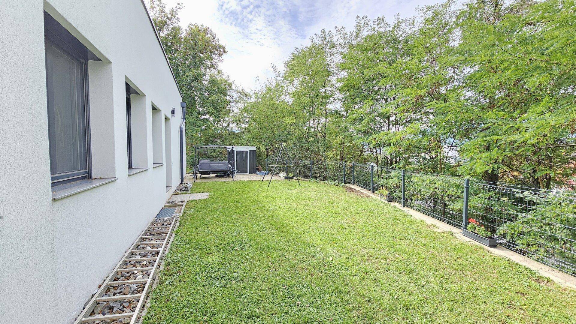 Gepflegter Garten mit Rasen, Gartenhaus und Schaukelbereich.