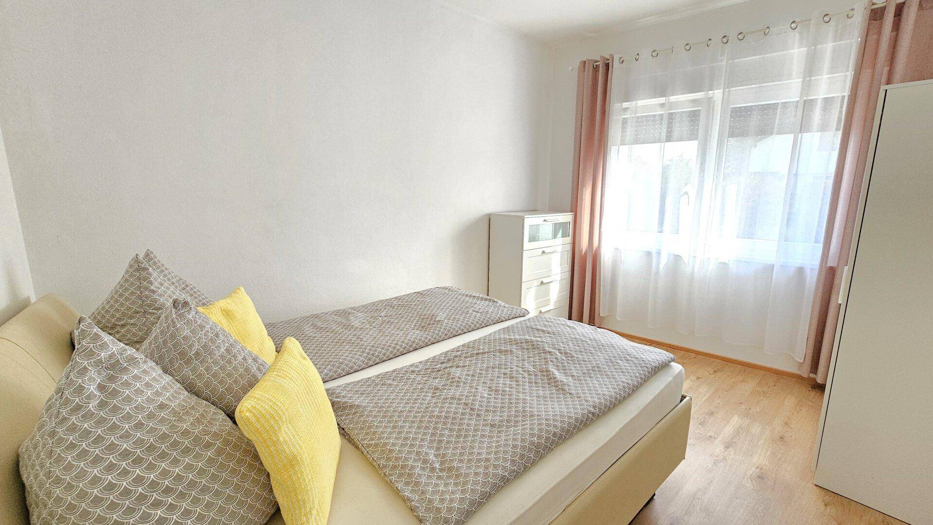 Schlafzimmer mit Einzelbetten, Holzboden und hellen Vorhängen.
