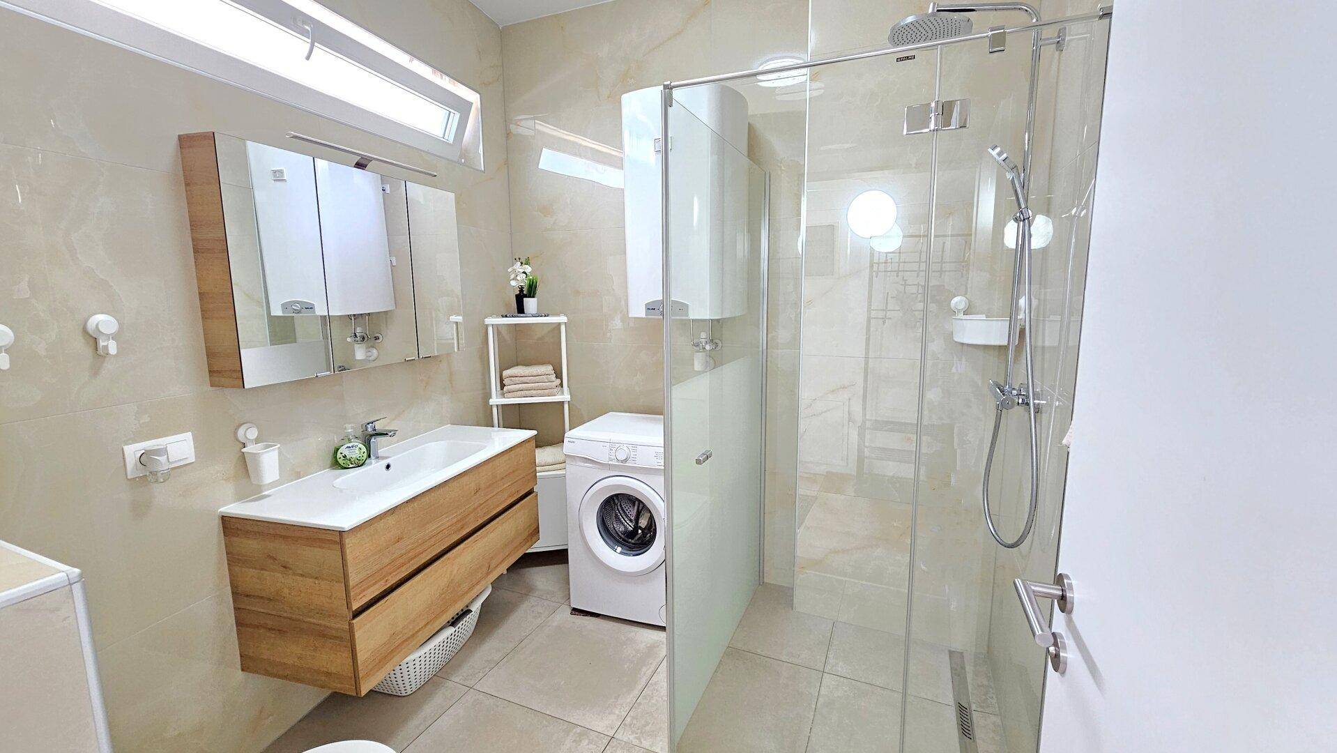 Modernes Badezimmer mit begehbarer Dusche, Waschmaschine und Holzwaschtisch.