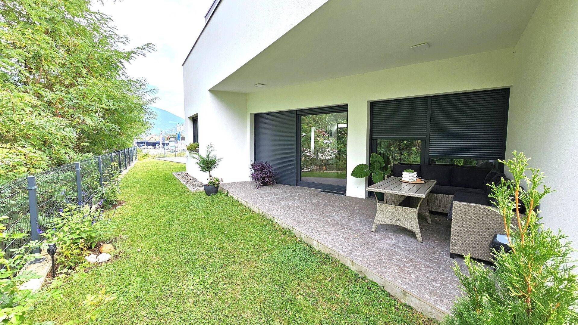 Überdachte Terrasse mit Sitzgelegenheiten, Rasenfläche und Zugang zum Garten.