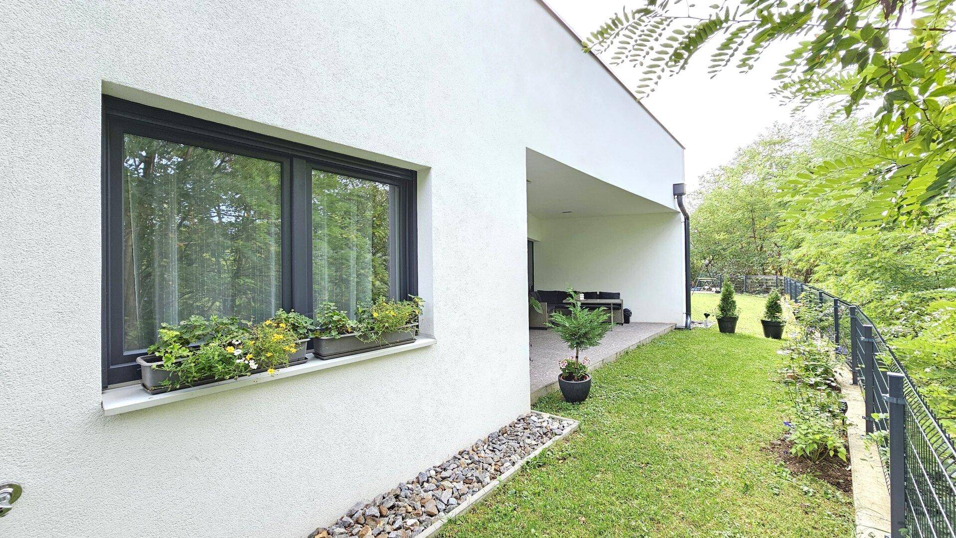 Seitenansicht des Hauses mit Fenster, Blumenkästen und angrenzendem Garten.
