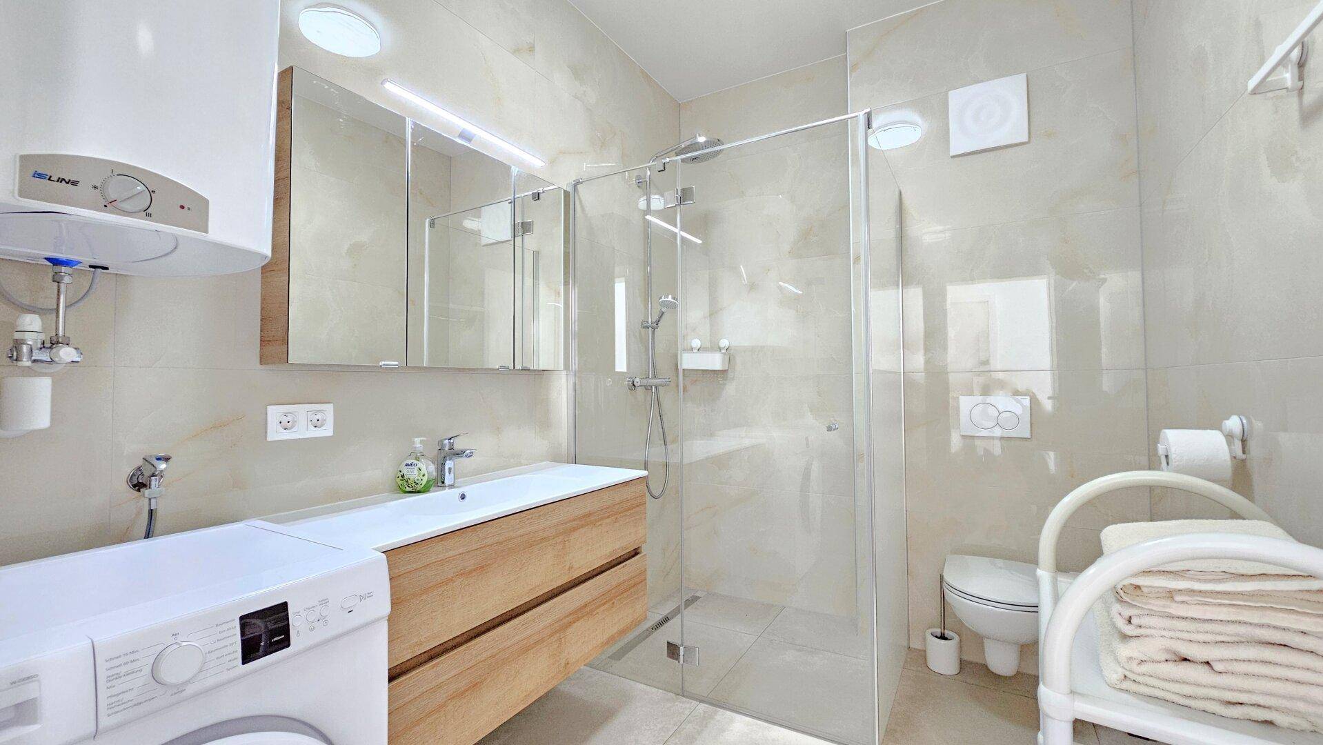 Modernes Badezimmer mit Duschkabine, Waschmaschine und Holzwaschtisch.