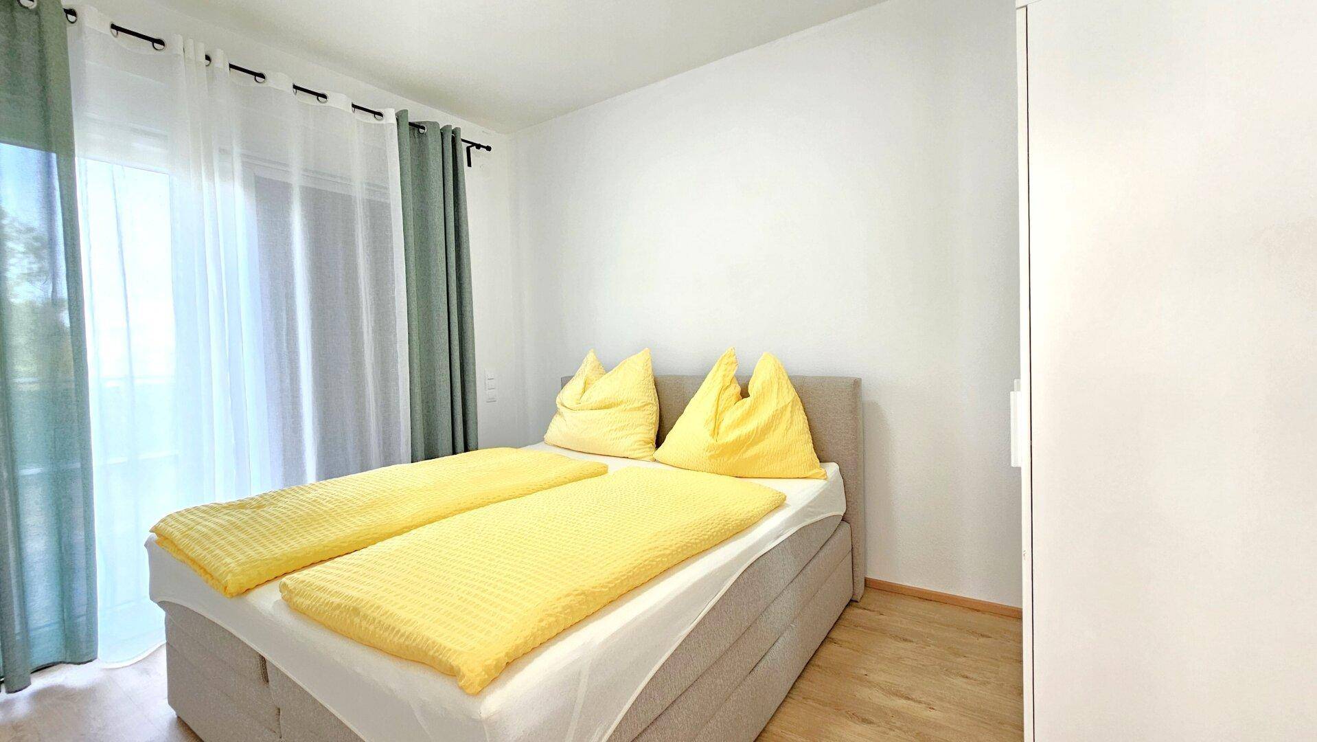 Schlafzimmer mit Doppelbett, Holzboden und hellen Vorhängen.