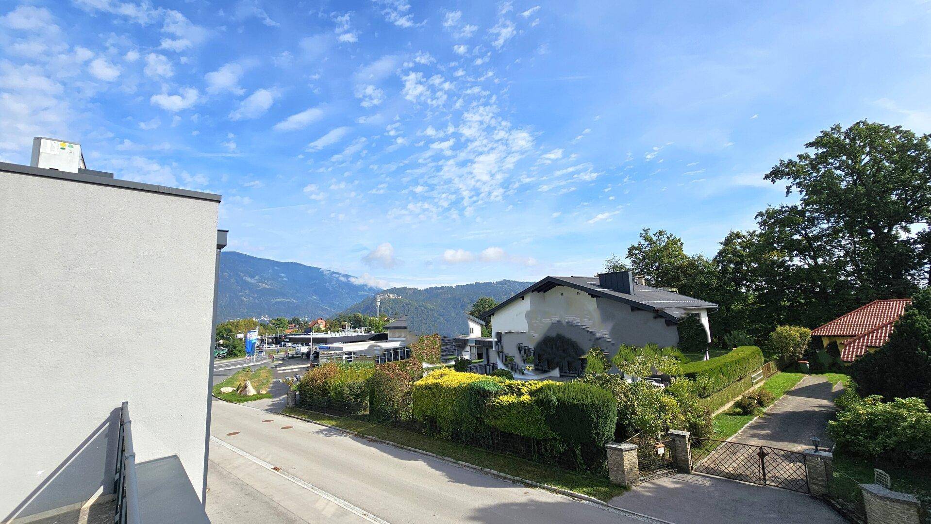 Weitläufiger Blick auf die Umgebung mit Bergen und Häusern unter blauem Himmel.