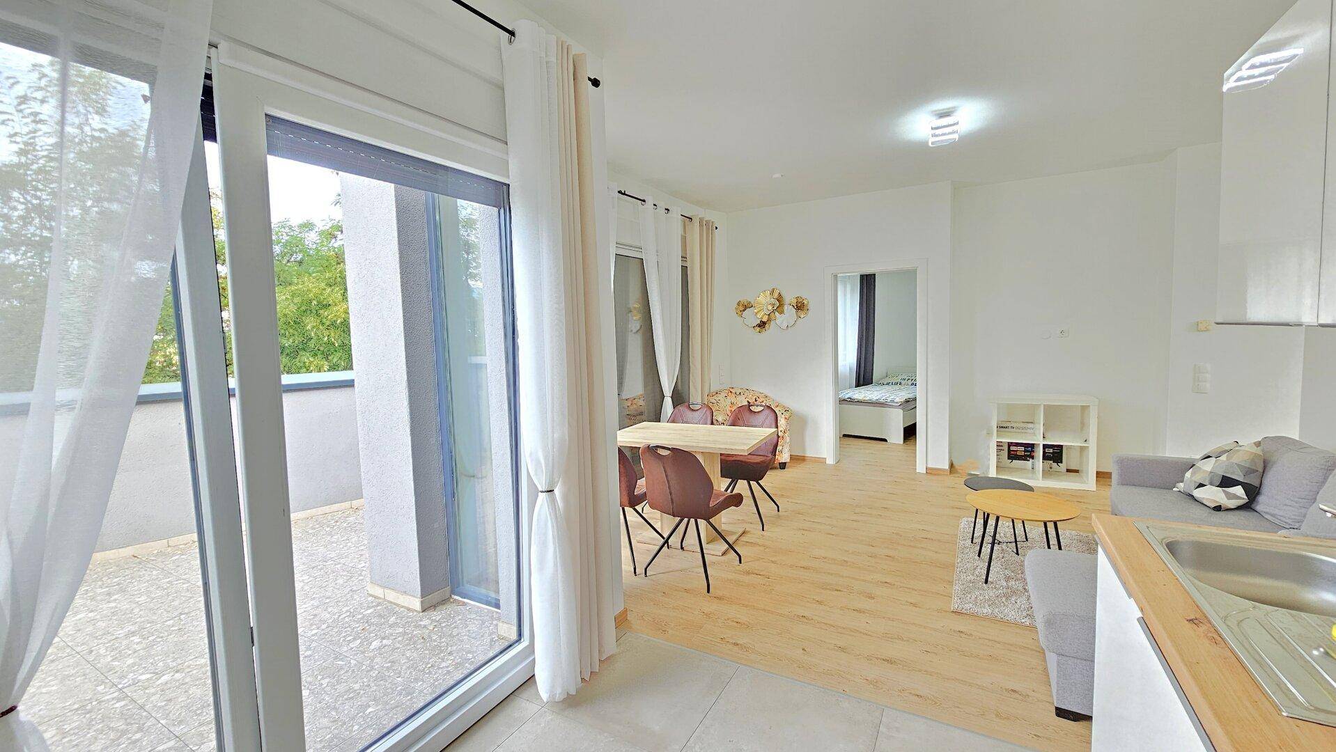 Offener Wohnbereich mit Essplatz, Sofa und Schiebetür zur Terrasse.